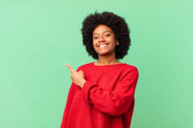 Afro siyah kadın neşeyle gülümsüyor, mutlu hissediyor ve yan ve yukarı doğru işaret ediyor, kopya uzayda nesne gösteriyor
