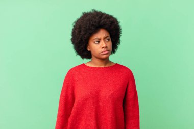 Afro siyahi kadın üzgün, üzgün ya da kızgın hissediyor ve olumsuz bir tavırla yan yana bakıyor, anlaşmazlık içinde kaşlarını çatıyor.