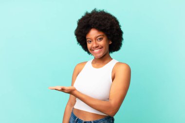 Afro siyah kadın neşeli bir şekilde gülümsüyor, mutlu hissediyor ve fotokopi uzayında bir konsept gösteriyor.