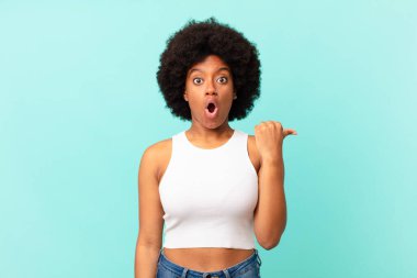 Afro siyah kadın inançsızlıktan şaşkın şaşkın bakıyor, yan taraftaki objeyi işaret ediyor ve diyor ki: