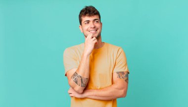 Yakışıklı bir adam mutlu, kendinden emin bir ifadeyle gülümsüyor. Elleri çenesinde, merak ediyor ve yan tarafa bakıyor.