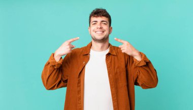 Yakışıklı adam kendinden emin bir şekilde gülümsüyor. Geniş bir gülümseme, pozitif, rahat, tatmin olmuş bir tavır sergiliyor.