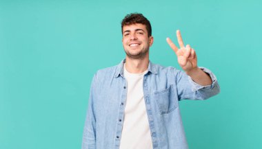 Yakışıklı adam gülümsüyor ve mutlu görünüyor, kaygısız ve pozitif, işaret eden zafer ya da barış tek elle