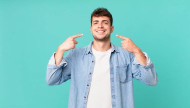 Yakışıklı adam kendinden emin bir şekilde gülümsüyor. Geniş bir gülümseme, pozitif, rahat, tatmin olmuş bir tavır sergiliyor.