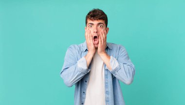 Yakışıklı adam şok olmuş ve korkmuş hissediyor, ağzı açık ve elleri yanaklarında korkmuş görünüyor.