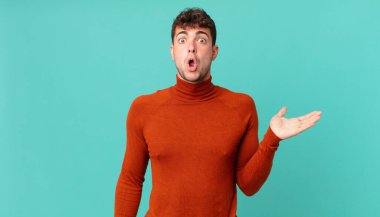 Yakışıklı adam şaşırmış ve şoka uğramış görünüyor, çenesi düşmüş, bir objeyi elinde açık bir elle tutuyor.