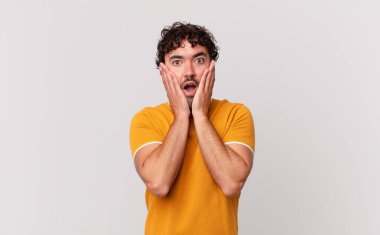İspanyol yakışıklı adam şok olmuş ve korkmuş hissediyor, ağzı açık ve elleri yanaklarında korkmuş görünüyor.