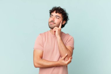 İspanyol yakışıklı adam mutlu bir şekilde gülümsüyor ve hayal kuruyor ya da şüphe ediyor, yana bakıyor.