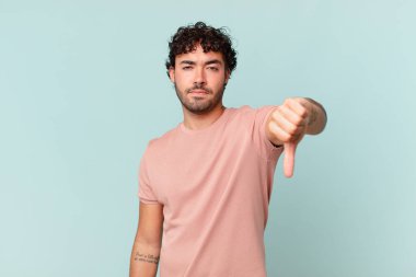 İspanyol yakışıklı adam sinirli, sinirli, sinirli, hayal kırıklığına uğramış ya da hoşnutsuz, ciddi bir bakışla başparmağını kaldırıyor.