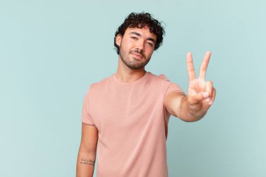 İspanyol yakışıklı adam gülümsüyor ve arkadaş canlısı görünüyor. İki ya da iki numarayı gösteriyor. Elleri önde, geriye doğru sayıyor.