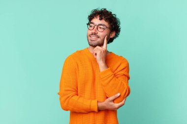 İspanyol yakışıklı adam mutlu bir şekilde gülümsüyor ve hayal kuruyor ya da şüphe ediyor, yana bakıyor.