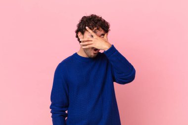 İspanyol yakışıklı adam şok olmuş, korkmuş ya da korkmuş görünüyor. Yüzü elle kaplanmış ve parmaklarının arasından gizlice bakıyor.