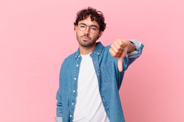 İspanyol yakışıklı adam sinirli, sinirli, sinirli, hayal kırıklığına uğramış ya da hoşnutsuz, ciddi bir bakışla başparmağını kaldırıyor.