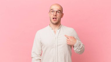 Şok olmuş ve ağzı açık, kendini işaret eden kel bir adam.