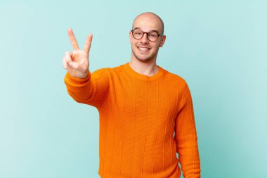 Kel adam gülümsüyor ve mutlu görünüyor, kaygısız ve pozitif, işaret eden zafer ya da barış tek elle