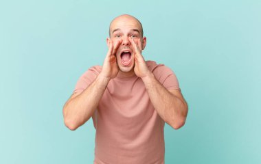 Kel adam mutlu, heyecanlı ve pozitif hissediyor. Elleri ağızda, bağırarak bağırıyor.