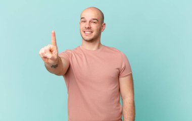 Kel adam gülümsüyor ve arkadaş canlısı görünüyor, bir numarayı gösteriyor ya da ilk eli önde, geriye doğru sayıyor.