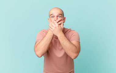 Kel adam elleri ile ağzını kapatıyor, şok olmuş, şaşırmış bir ifadeyle, sır saklıyor ya da 