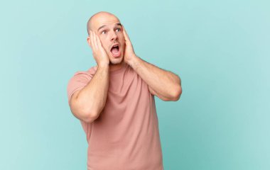 Kel adam mutlu, heyecanlı ve şaşırmış hissediyor, iki eli yüzü de havada bir tarafa bakıyor.