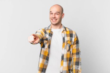 Kel adam kameraya bakıyor, tatmin olmuş, kendinden emin, dostane bir gülümsemeyle, seni seçiyor.