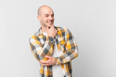 Kel adam mutlu, kendinden emin bir ifadeyle gülümsüyor, çenesinde elleri olan, merak eden ve yan tarafa bakan.