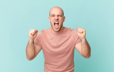 Kel adam öfkeli bir ifadeyle ya da yumruklarıyla başarıyı kutlarken agresif bir şekilde bağırıyor.