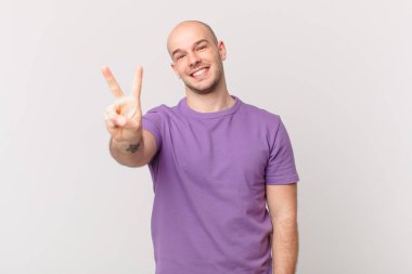 Kel adam gülümsüyor ve arkadaş canlısı görünüyor, iki ya da iki numarayı gösteriyor, eli önde, geriye doğru sayıyor.