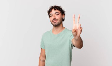 İspanyol yakışıklı adam gülümsüyor ve arkadaş canlısı görünüyor. İki ya da iki numarayı gösteriyor. Elleri önde, geriye doğru sayıyor.