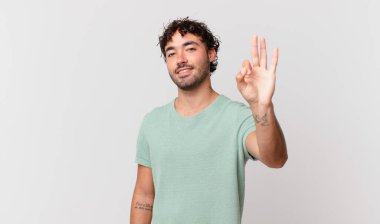 İspanyol yakışıklı adam gülümsüyor ve arkadaş canlısı görünüyor, üç ya da üç numarayı gösteriyor, eli önde, geriye doğru sayıyor.