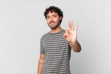 İspanyol yakışıklı adam gülümsüyor ve arkadaş canlısı görünüyor, üç ya da üç numarayı gösteriyor, eli önde, geriye doğru sayıyor.