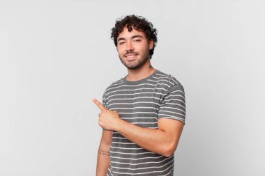 Hispanik yakışıklı adam neşeyle gülümsüyor, mutlu hissediyor ve kenarı ve yukarıyı işaret ediyor, fotokopi uzayında nesne gösteriyor