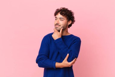 İspanyol yakışıklı, gülümseyen mutlu, kendine güvenen, eli çenesinde, merak eden ve yan tarafa bakan bir adam.