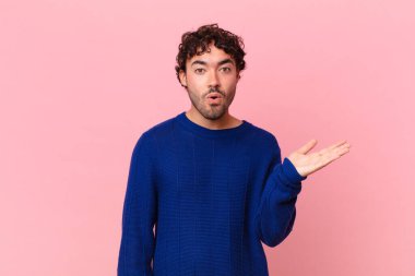 İspanyol yakışıklı adam şaşırmış ve şoka uğramış görünüyor, çenesi düşmüş, bir objeyi elinde açık bir elle tutuyor.