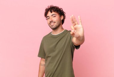 İspanyol yakışıklı adam gülümsüyor ve arkadaş canlısı görünüyor, üç ya da üç numarayı gösteriyor, eli önde, geriye doğru sayıyor.