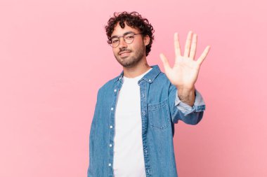 İspanyol yakışıklı adam gülümsüyor ve arkadaş canlısı görünüyor, 5 ya da 5 numarayı gösteriyor, elleri önde, geri sayıyor.