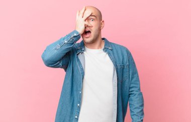 Kel adam şok olmuş, korkmuş ya da korkmuş görünüyor. Yüzü elle örtülmüş ve parmaklarının arasından gizlice bakıyor.