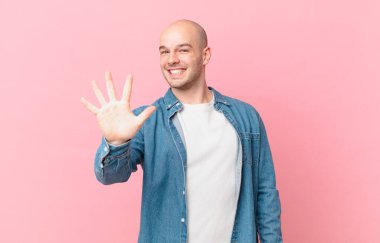 Kel adam gülümsüyor ve dost canlısı görünüyor. 5 ya da 5 numarayı gösteriyor. Eli önde, geriye doğru sayıyor.