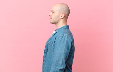 Kel adam profil görünümünde. İlerideki boşluğu kopyalamak istiyor. Düşünüyor, hayal ediyor ya da hayal ediyor.