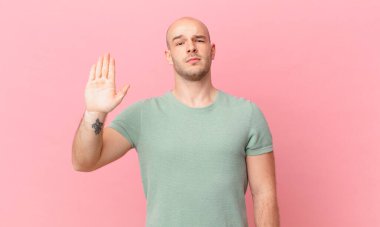 Kel adam ciddi, sert, hoşnutsuz ve kızgın görünüyor. Avuç içini açıp jesti durduruyor.