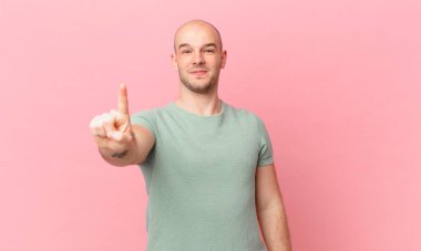 Kel adam gururla gülümsüyor ve gururla bir numaralı pozunu veriyor, kendini lider gibi hissediyor.