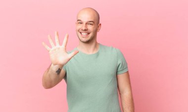 Kel adam gülümsüyor ve dost canlısı görünüyor. 5 ya da 5 numarayı gösteriyor. Eli önde, geriye doğru sayıyor.