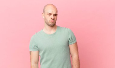 Kel bir adam üzgün, üzgün ya da kızgın. Olumsuz bir tavır sergiliyor, anlaşmazlık içinde kaşlarını çatıyor.