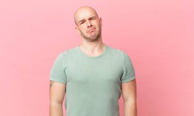 Kafası karışmış, kafası karışmış, sinirsel bir hareketle dudağını ısıran, sorunun cevabını bilmeyen kel bir adam.