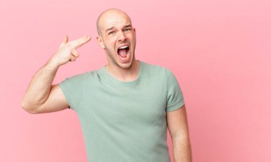 Kel adam mutsuz ve stresli görünüyor, intihar jesti elle silah işareti yapıyor, kafasını işaret ediyor.