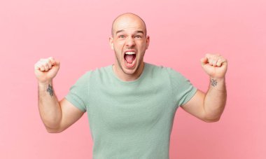 Kel adam öfkeli bir ifadeyle ya da yumruklarıyla başarıyı kutlarken agresif bir şekilde bağırıyor.