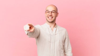 Kel adam kameraya bakıyor, tatmin olmuş, kendinden emin, dostane bir gülümsemeyle, seni seçiyor.