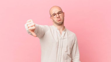 Kel bir adam kızgın, sinirli, hayal kırıklığına uğramış ya da canı sıkkın, ciddi bir bakışla başparmağını kaldırıyor.