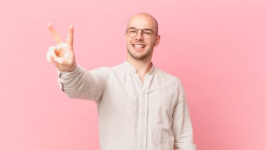 Kel adam gülümsüyor ve mutlu görünüyor, kaygısız ve pozitif, işaret eden zafer ya da barış tek elle