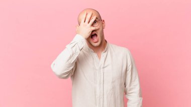 Kel adam şok olmuş, korkmuş ya da korkmuş görünüyor. Yüzü elle örtülmüş ve parmaklarının arasından gizlice bakıyor.