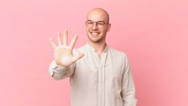 Kel adam gülümsüyor ve dost canlısı görünüyor. 5 ya da 5 numarayı gösteriyor. Eli önde, geriye doğru sayıyor.